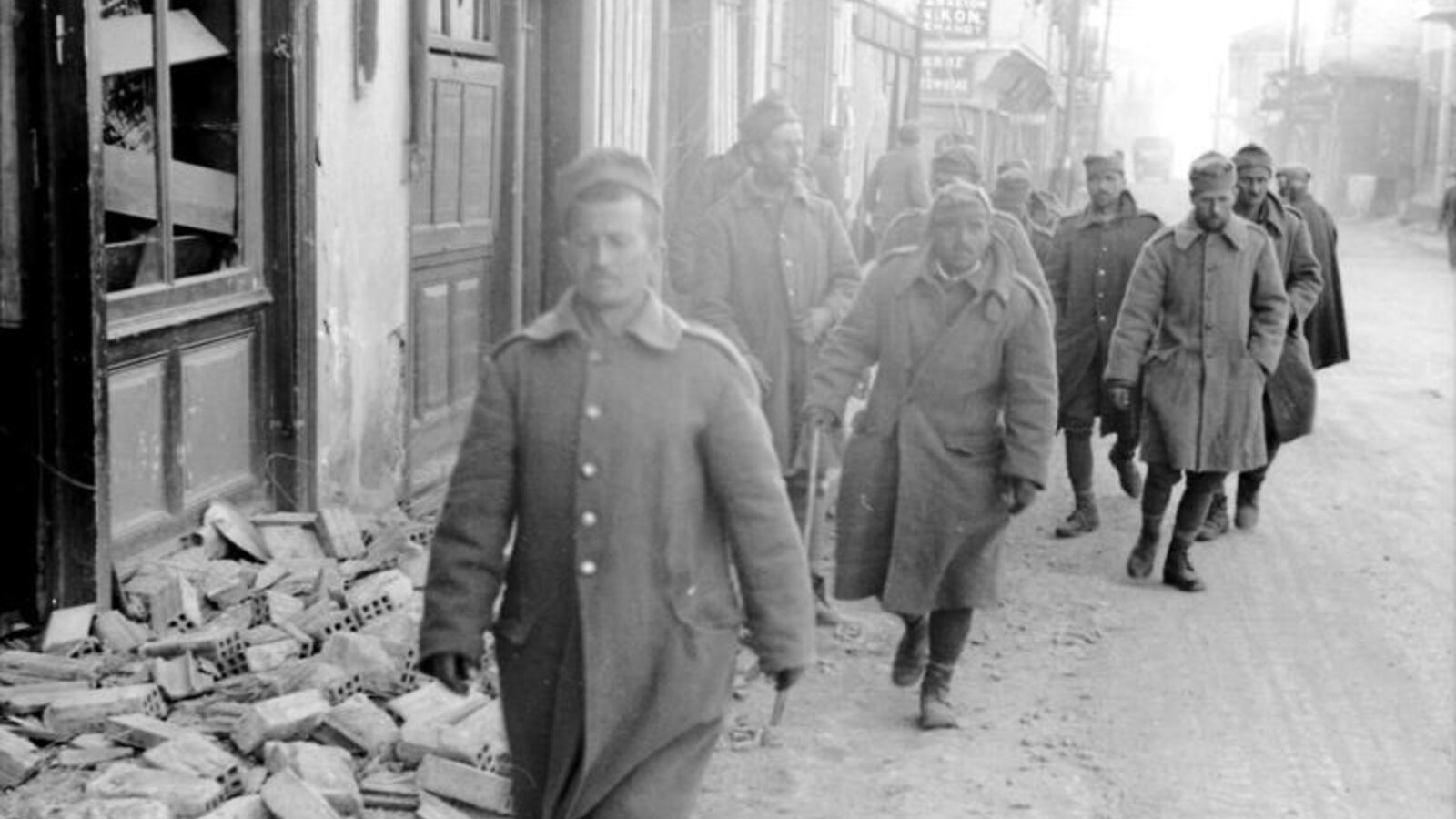 Greek soldiers walking along a street in a damaged village during the German invasion of Greece, April 1941